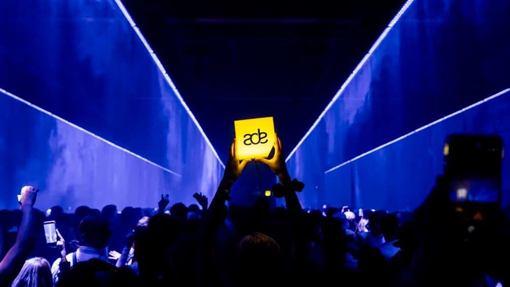 An ADE lightbox held above a crowd in a blue-lit venue