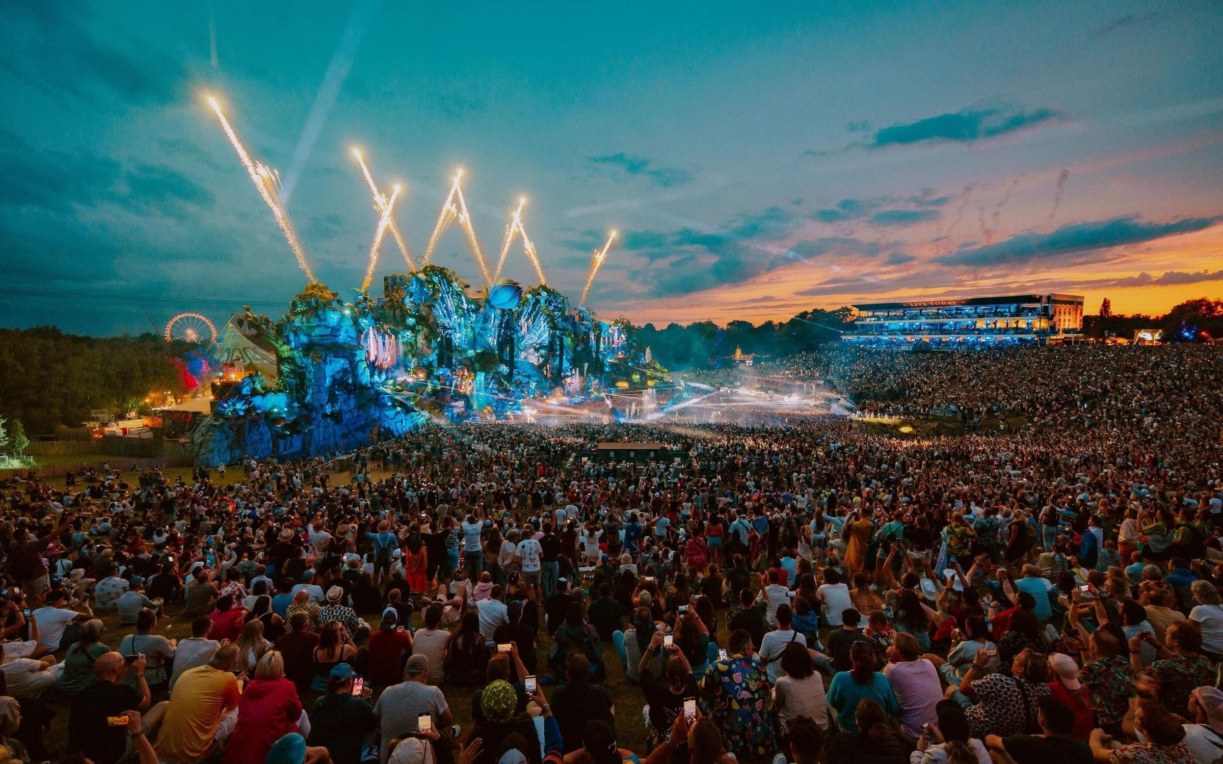 Large crowd at Tomorrowland festival in Belgium with massive stage production, fireworks, and thousands of electronic music fans during a summer techno festival.