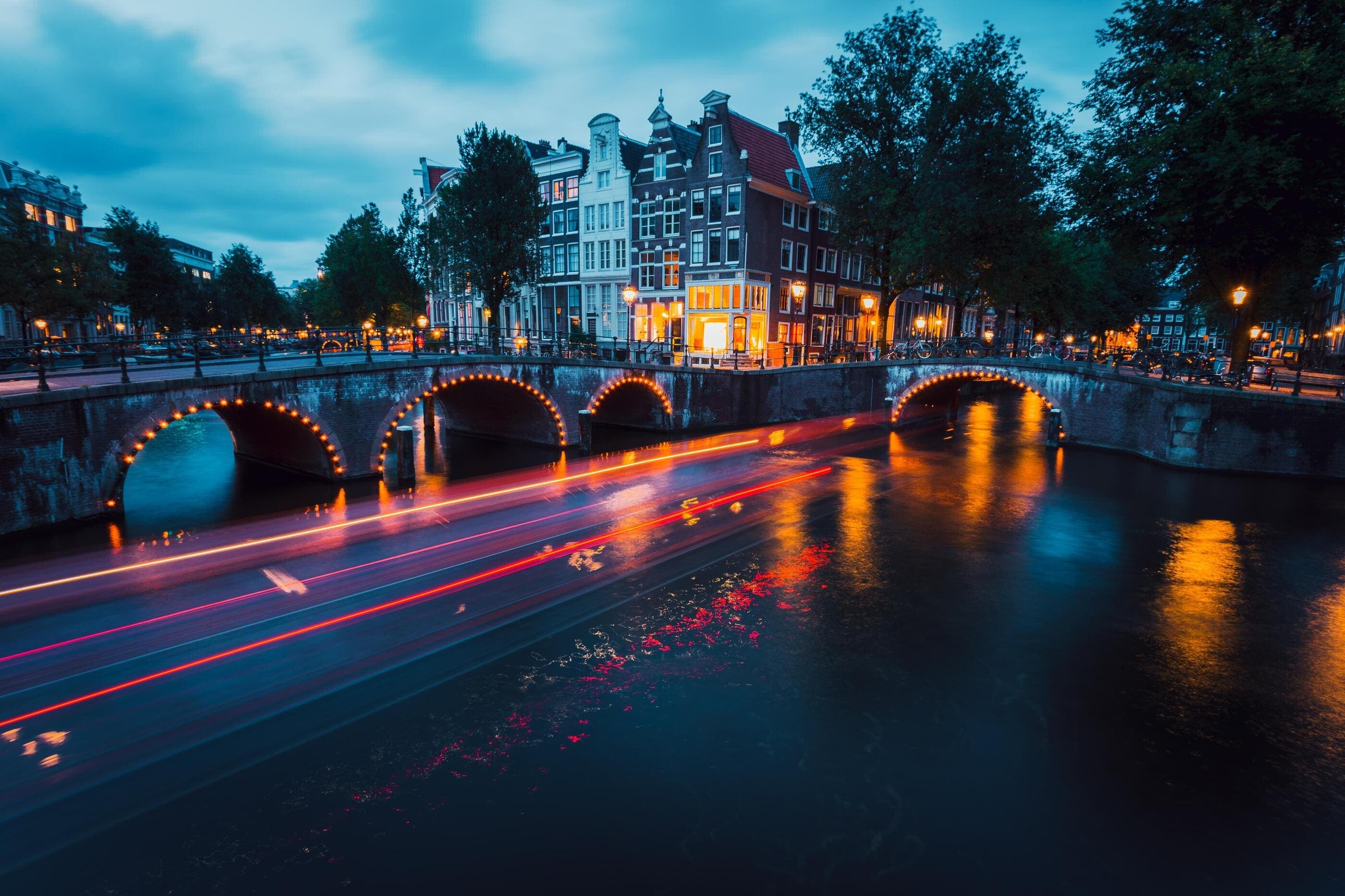 Night view of Amsterdam canals with illuminated bridges and historic buildings, reflecting the city’s atmosphere and nightlife culture.